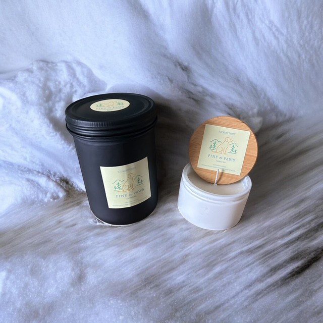 Two scented candles, one black and one white, on a soft fabric surface.