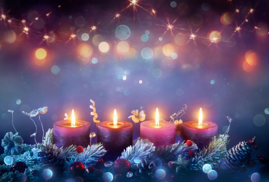 Four lit purple candles surrounded by festive decorations and lights.