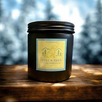 A black candle jar labeled "Fireside" on a wooden surface with a blurred snowy background.