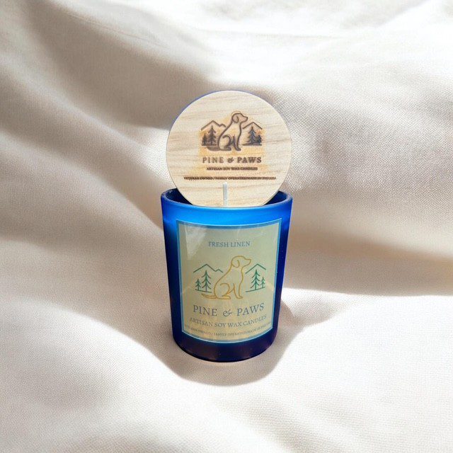 Blue glass jar candle with a wooden lid, placed on white fabric.