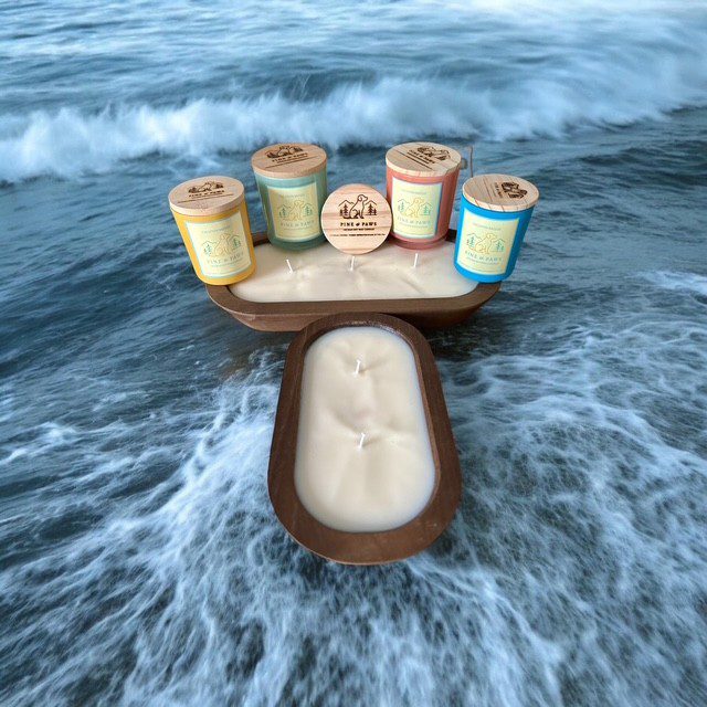 Ice cream cups and a popsicle on a wooden board by the ocean.